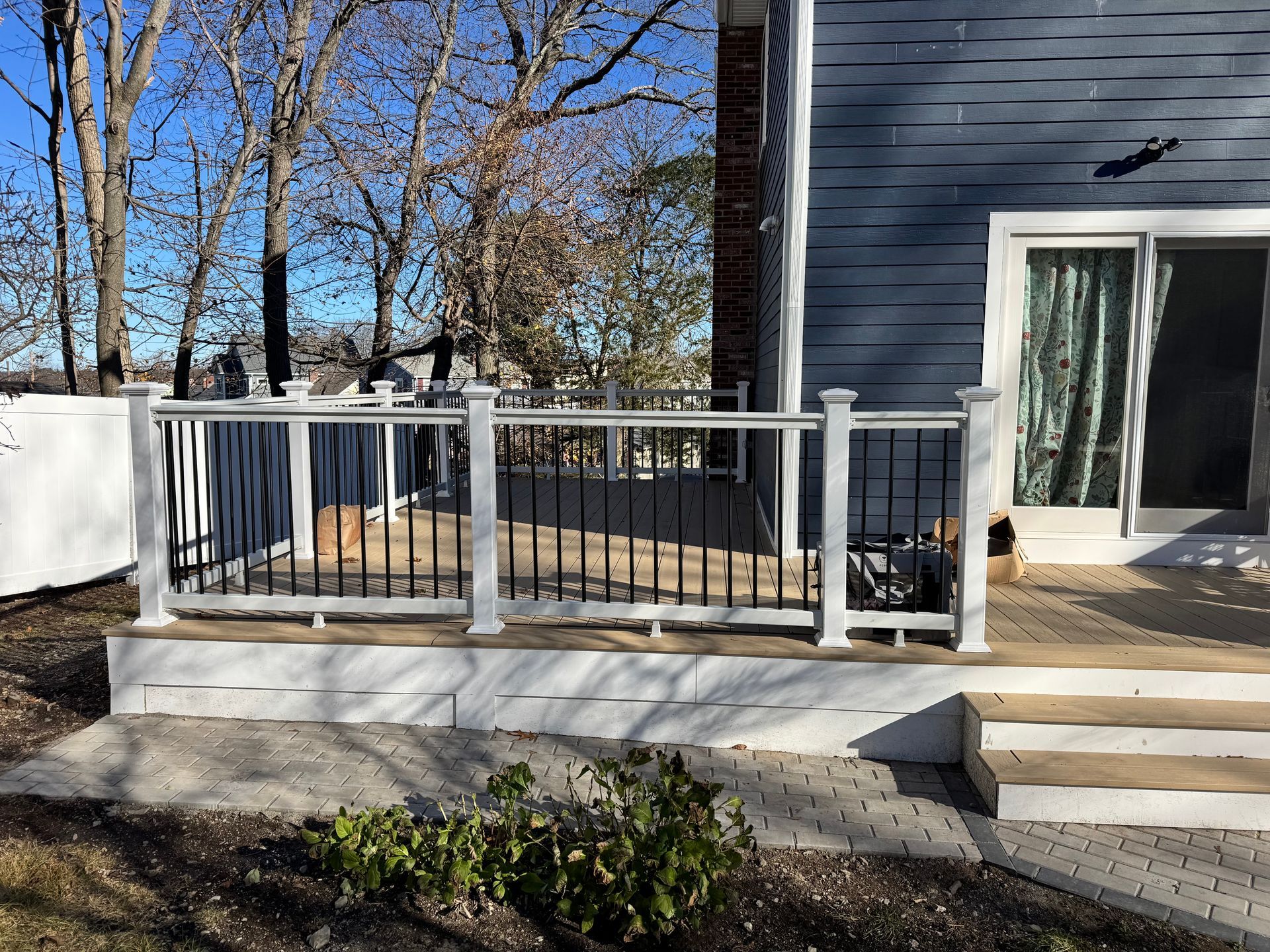 Deck with white posts and black railings, attached to a blue house with a sliding glass door.