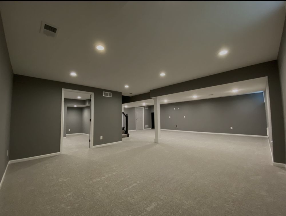 Empty gray basement with carpet, recessed lighting, and support columns.