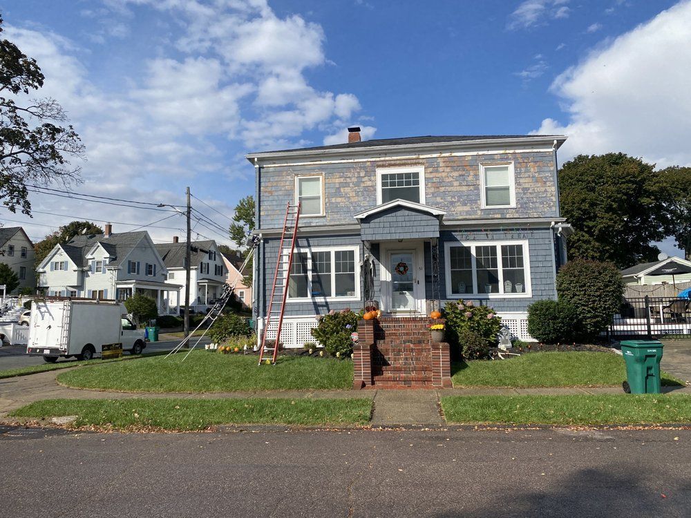 Two-story blue house under renovation, ladder against the side. Sunny day.