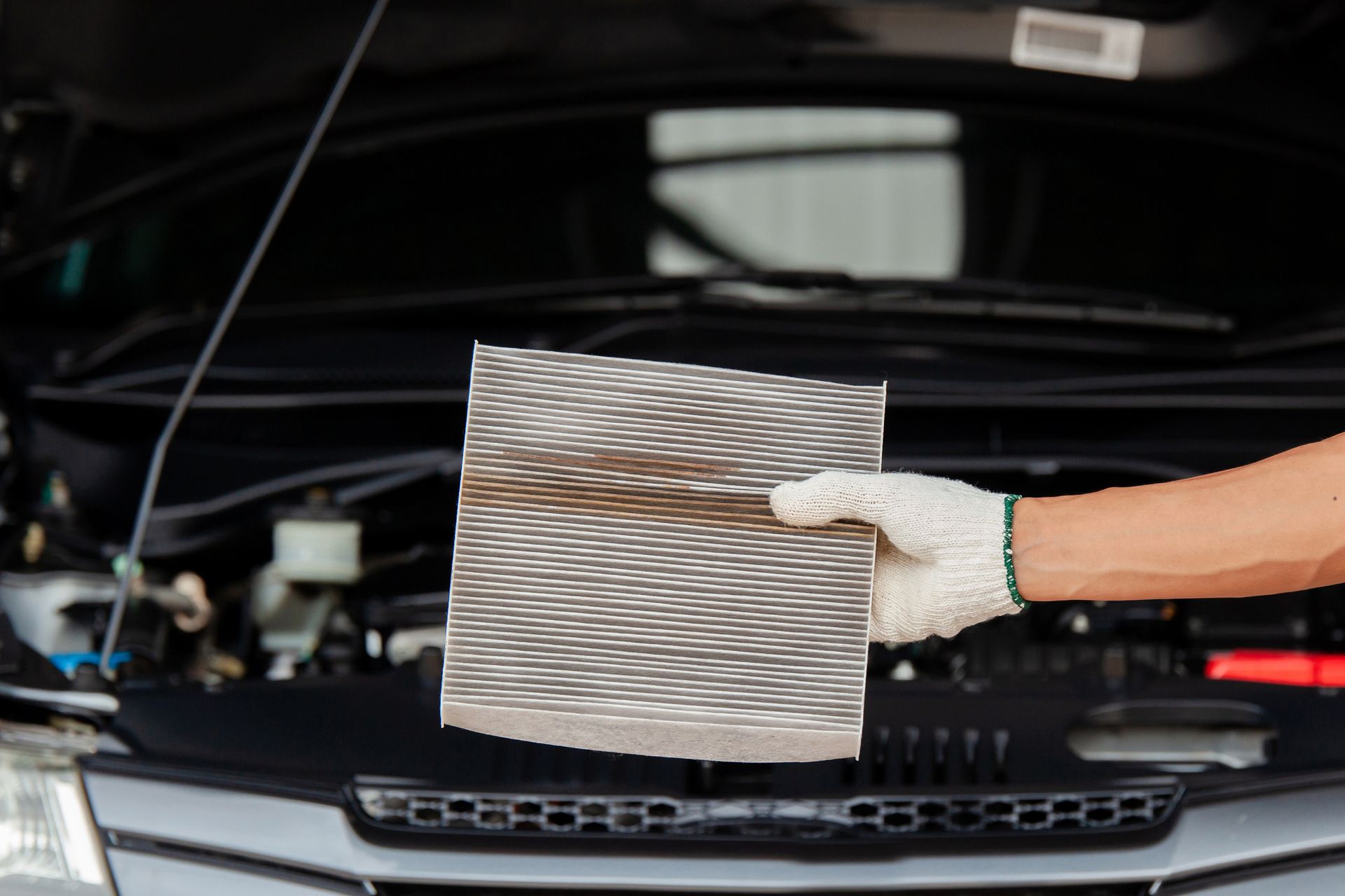 A person is holding a piece of paper in front of a car with the hood open.