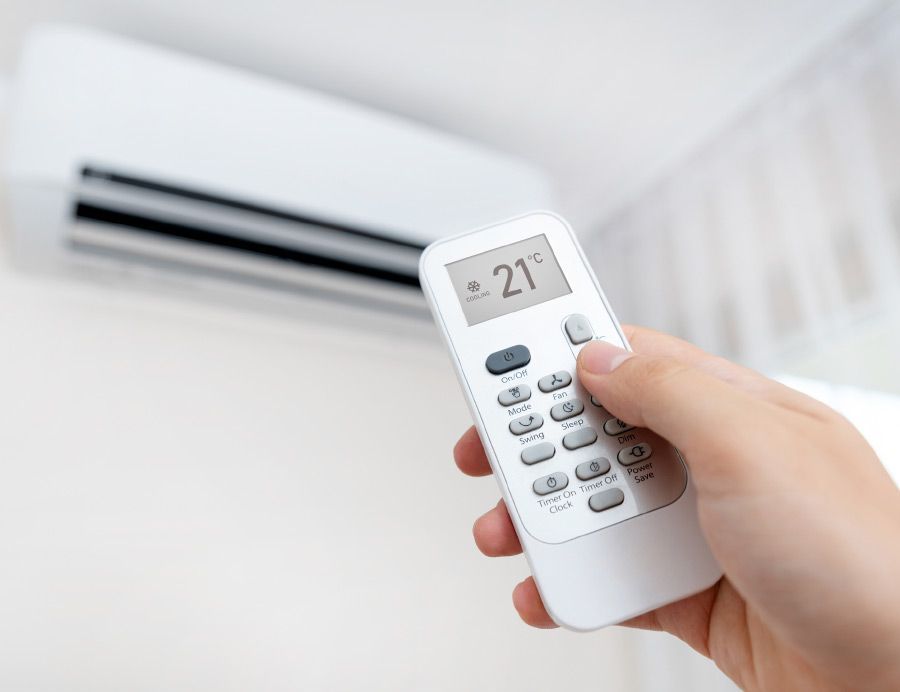 A person is holding a remote control in front of an air conditioner.