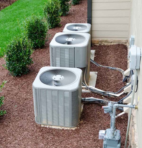 A row of air conditioners are sitting outside of a house.