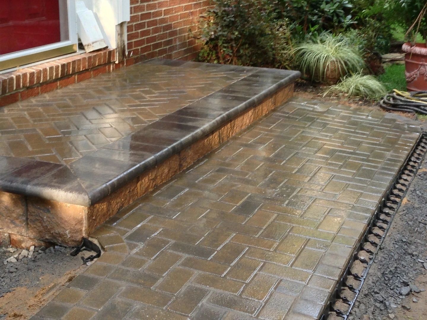 Brick walkway and step leading to a brick home entrance, wet from rain.