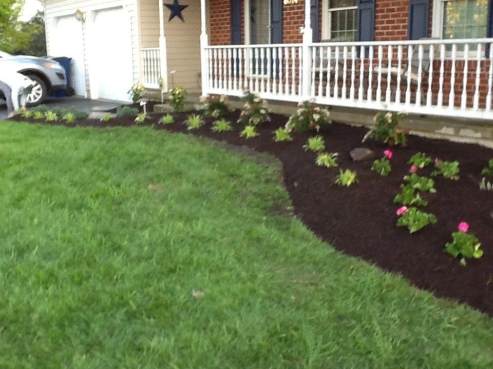 Well-manicured lawn and flower bed in front of a house with a white porch.