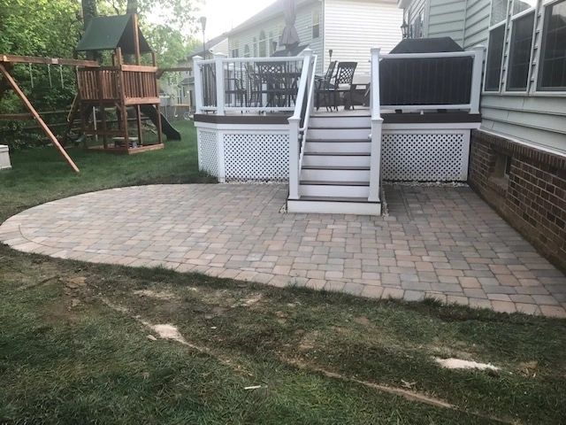 Brick patio in a backyard with a wooden deck and a play set.