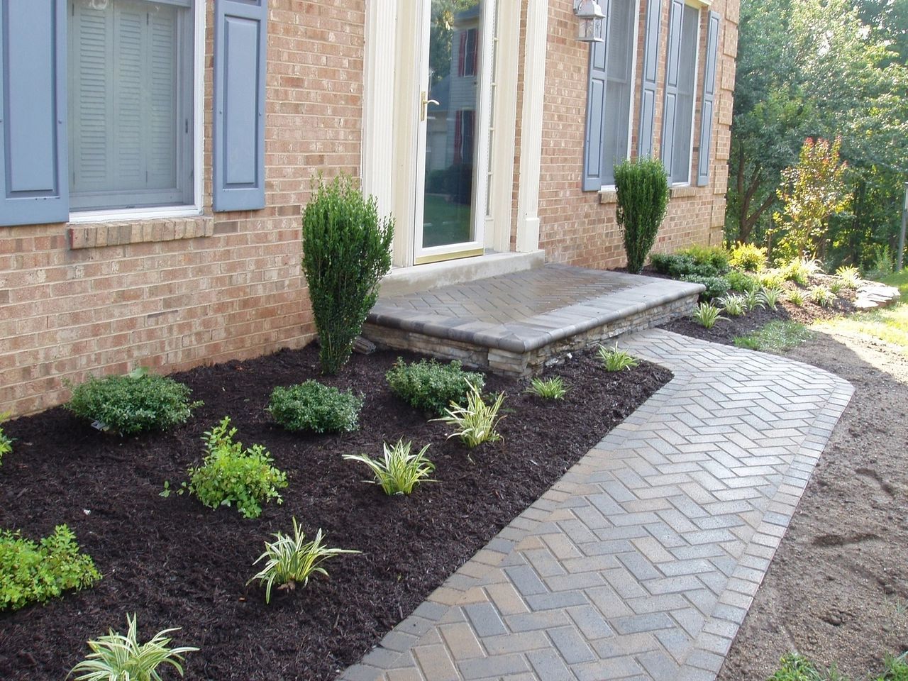 Brick house entrance with a brick walkway and landscaped flowerbed.