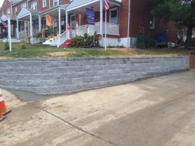 Gray retaining wall in front of brick houses, with a sloped driveway and grass.