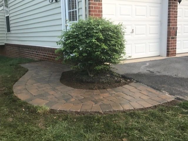 Brick pathway curves around a shrub, leading from the grass to a garage door.