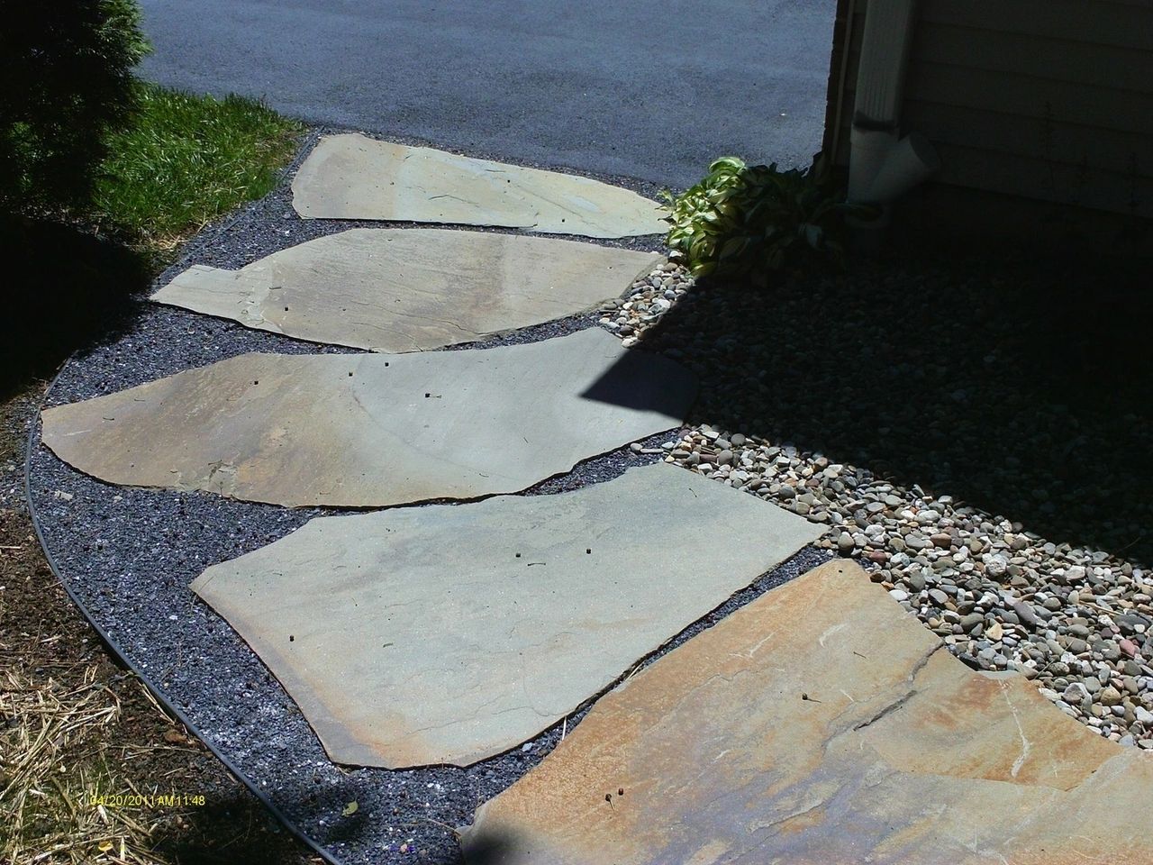 Stone pathway leading to a building's entrance, surrounded by dark gravel and grass.