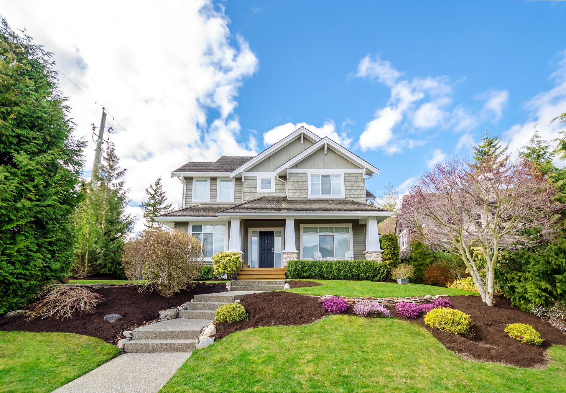 Two-story house with light gray siding, white trim, and a well-manicured lawn under a blue sky.