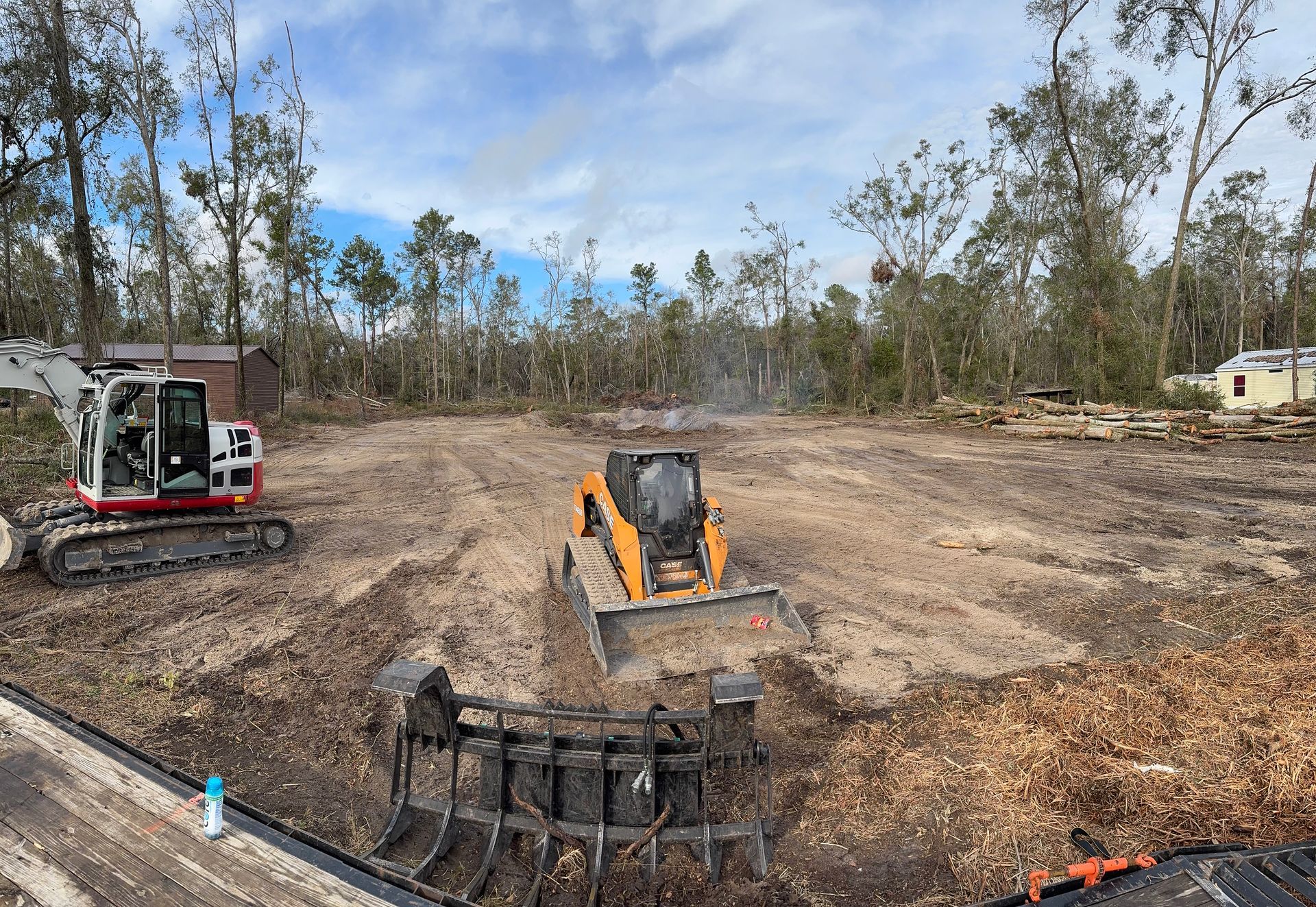 Excavator and skid steer clearing a lot of wood chips in a forest setting.