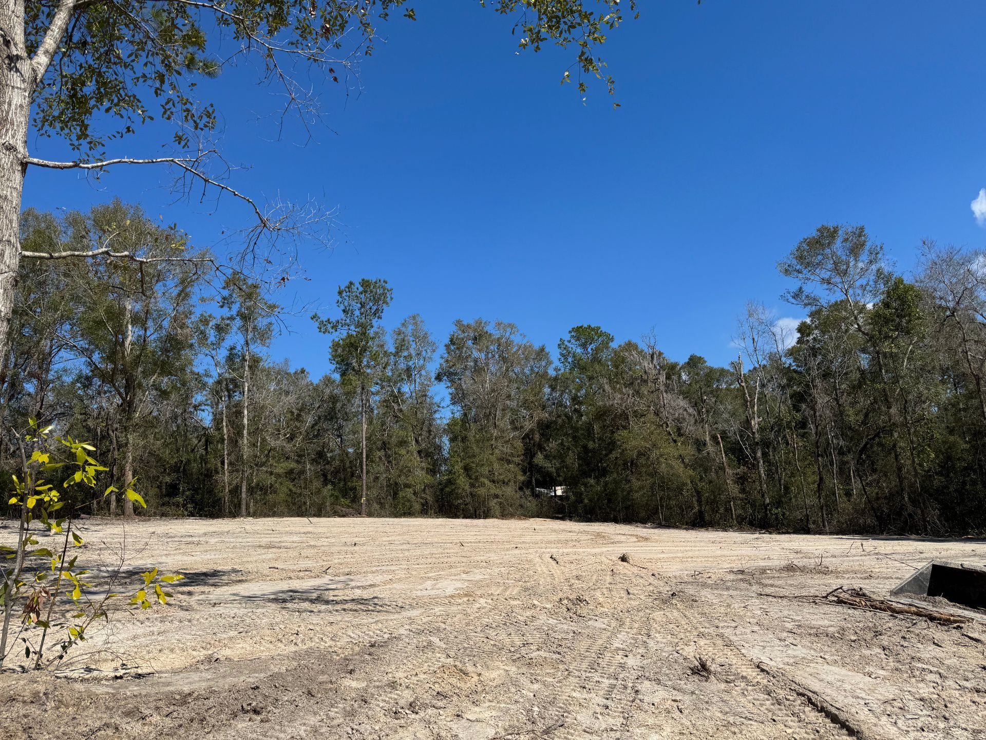 Cleared lot, likely for building, with a blue sky and trees in the background.