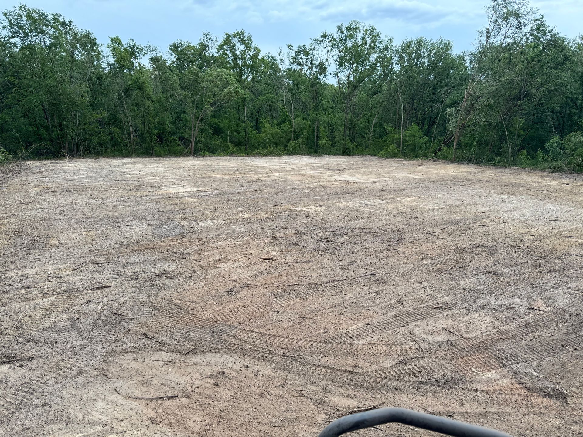 Clearing with dirt in the foreground, a forest in the background, on a cloudy day.