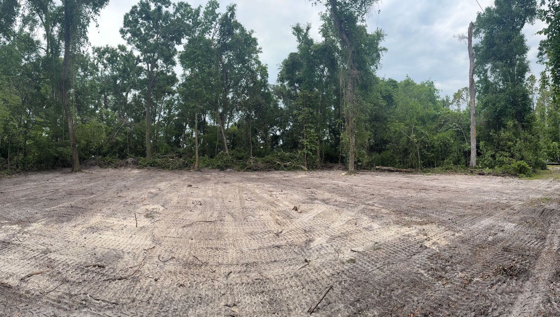 Cleared dirt lot with trees in the background; overcast sky.