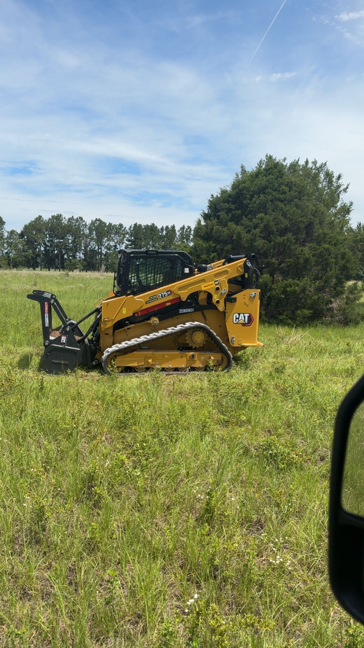 Yellow Caterpillar skid steer clearing vegetation in a grassy field.