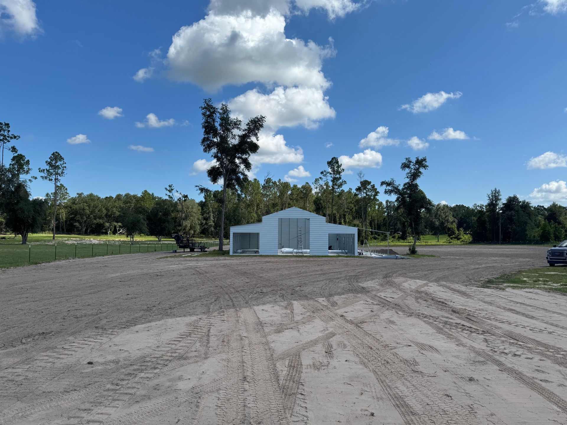 White building in a clearing, surrounded by dirt and trees, under a blue sky with clouds.