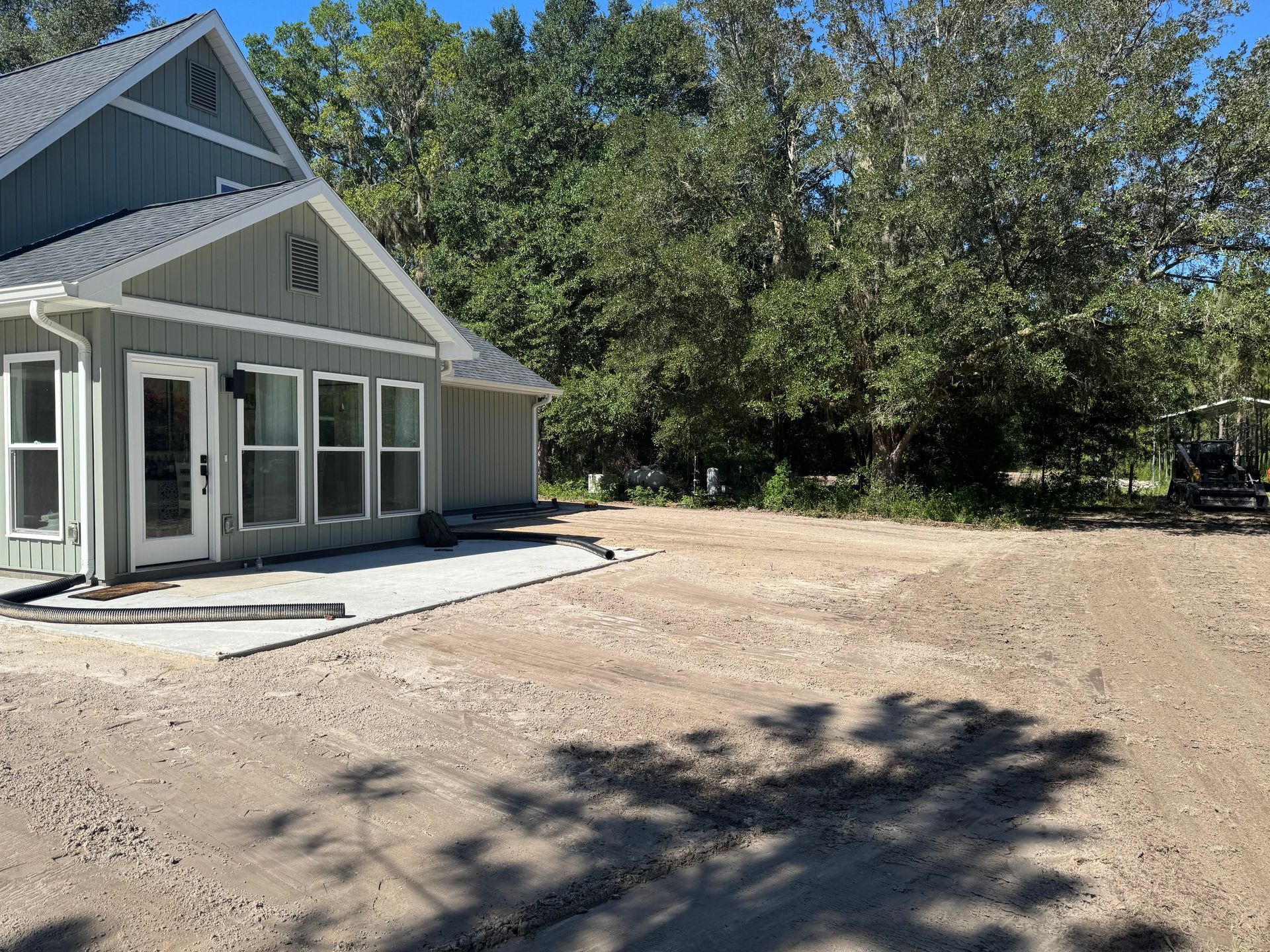 A light green house with large windows and a gravel yard, under a sunny sky.