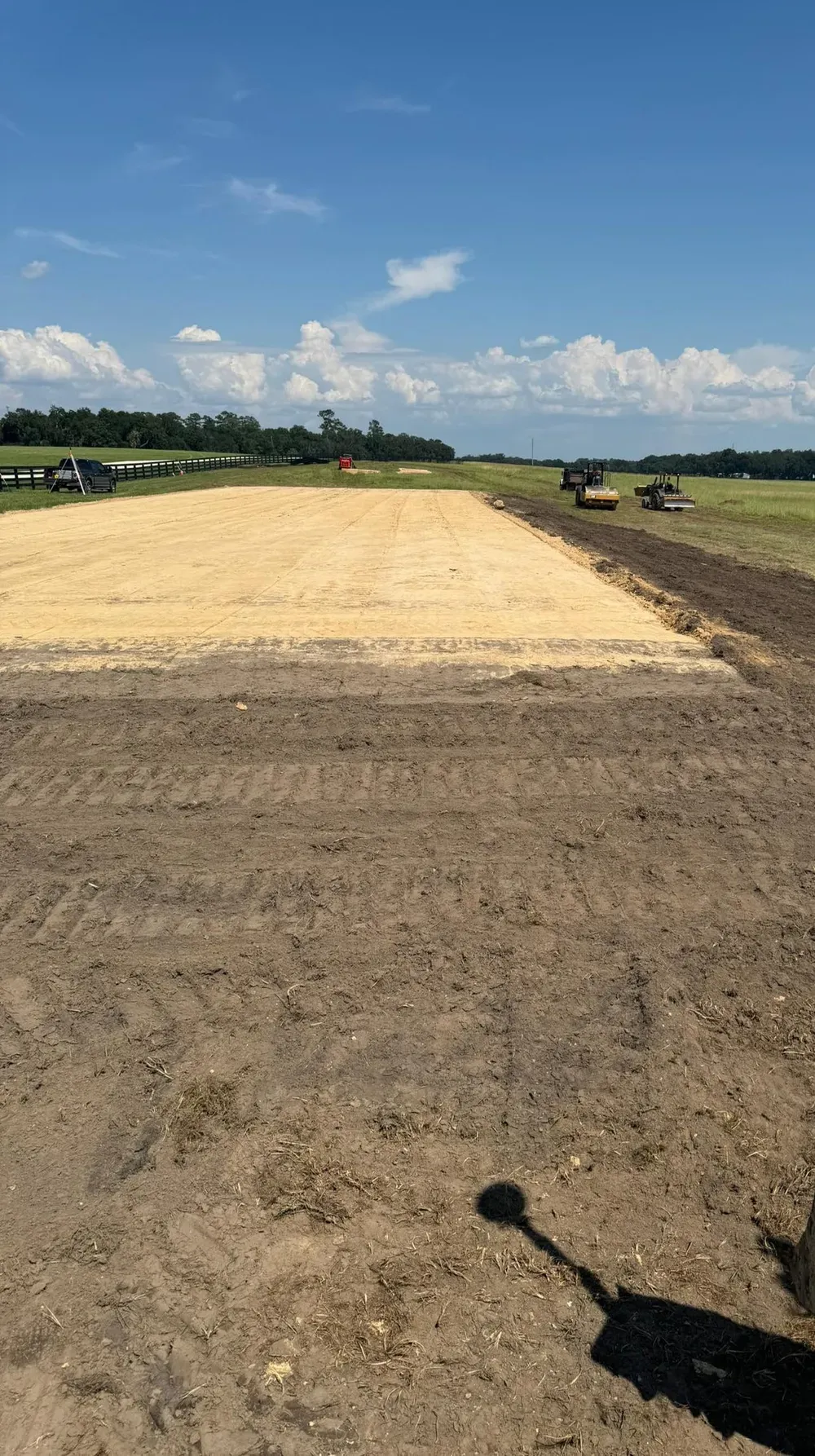 Construction site with graded dirt and sand, under a blue sky.