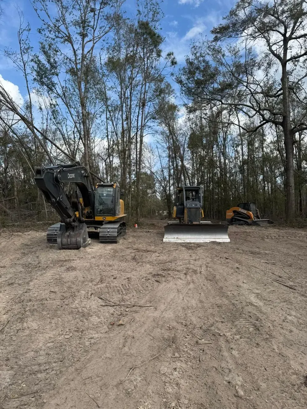 Heavy construction equipment in a clearing, trees in background, overcast sky.