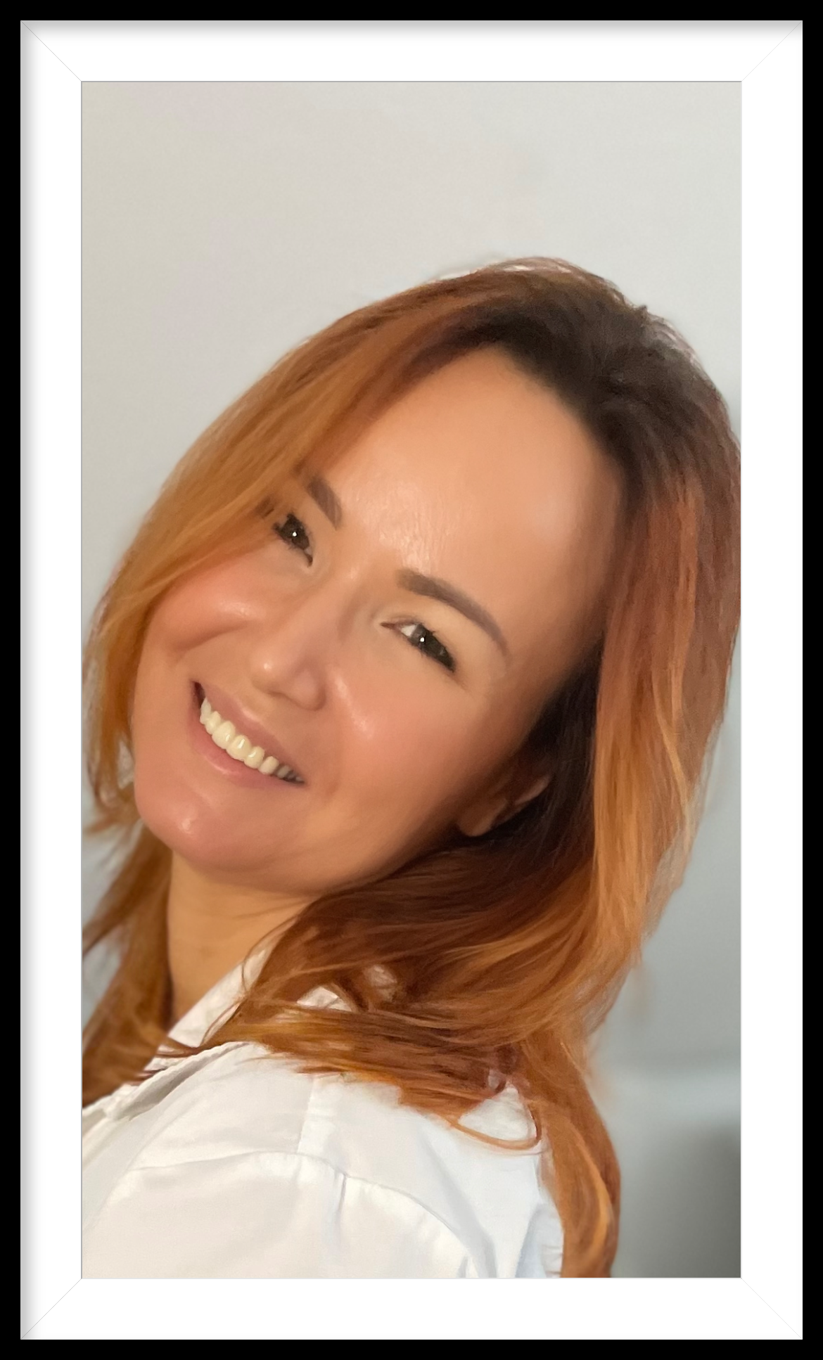Eine Frau mit roten Haaren trägt ein weißes Hemd und lächelt.