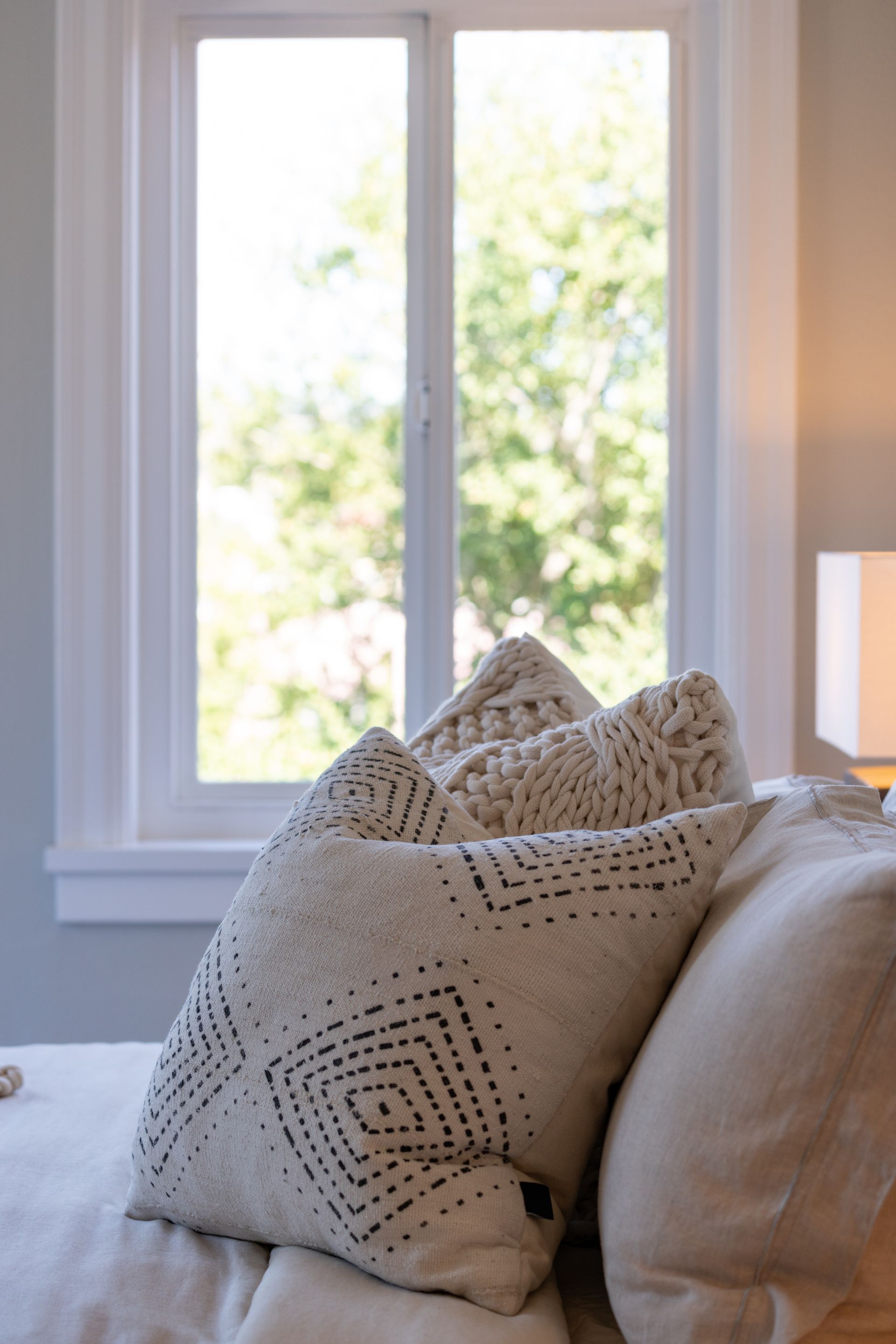 White patterned pillows on a bed beside a bright window in a sunlit bedroom