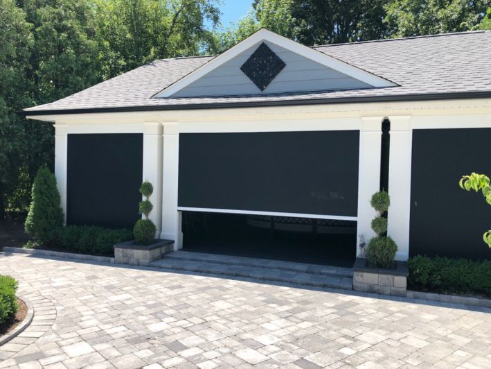 A white home has black patio shades on it's garage. 