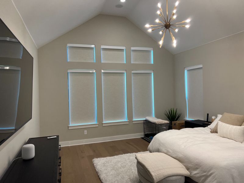 A bedroom has a wall of windows with automated window roller shades.
