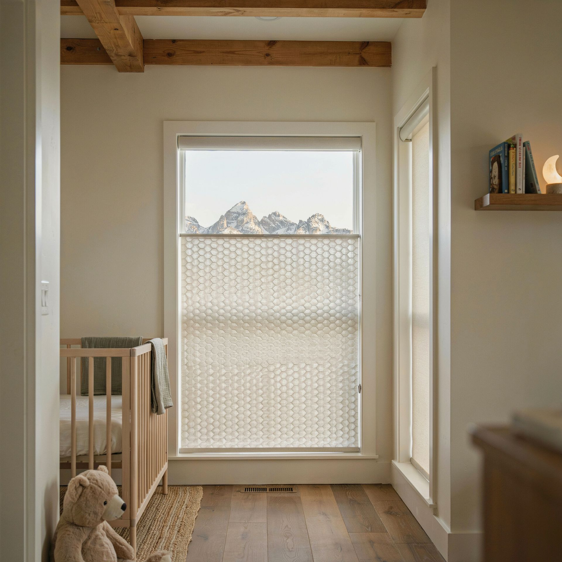 Bright nursery hallway with a teddy bear, crib, and window with top-down-bottom-up shades showing mountains.
