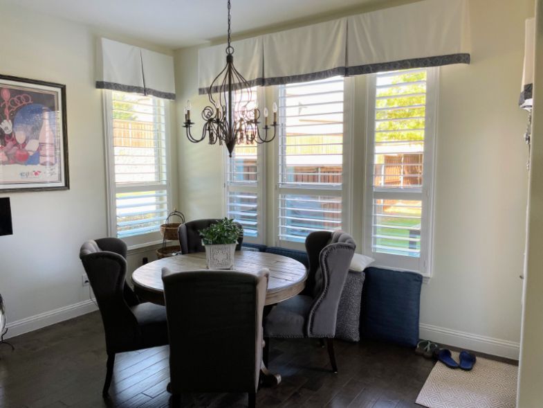 A dining room with a table and chairs, a chandelier, and shutters on the windows.