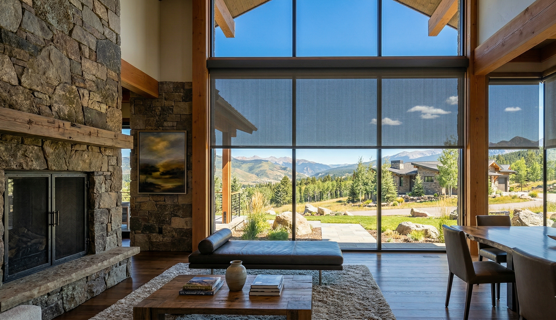 A rustic living room with a large stone fireplace, floor-to-ceiling windows, and a mountain view.