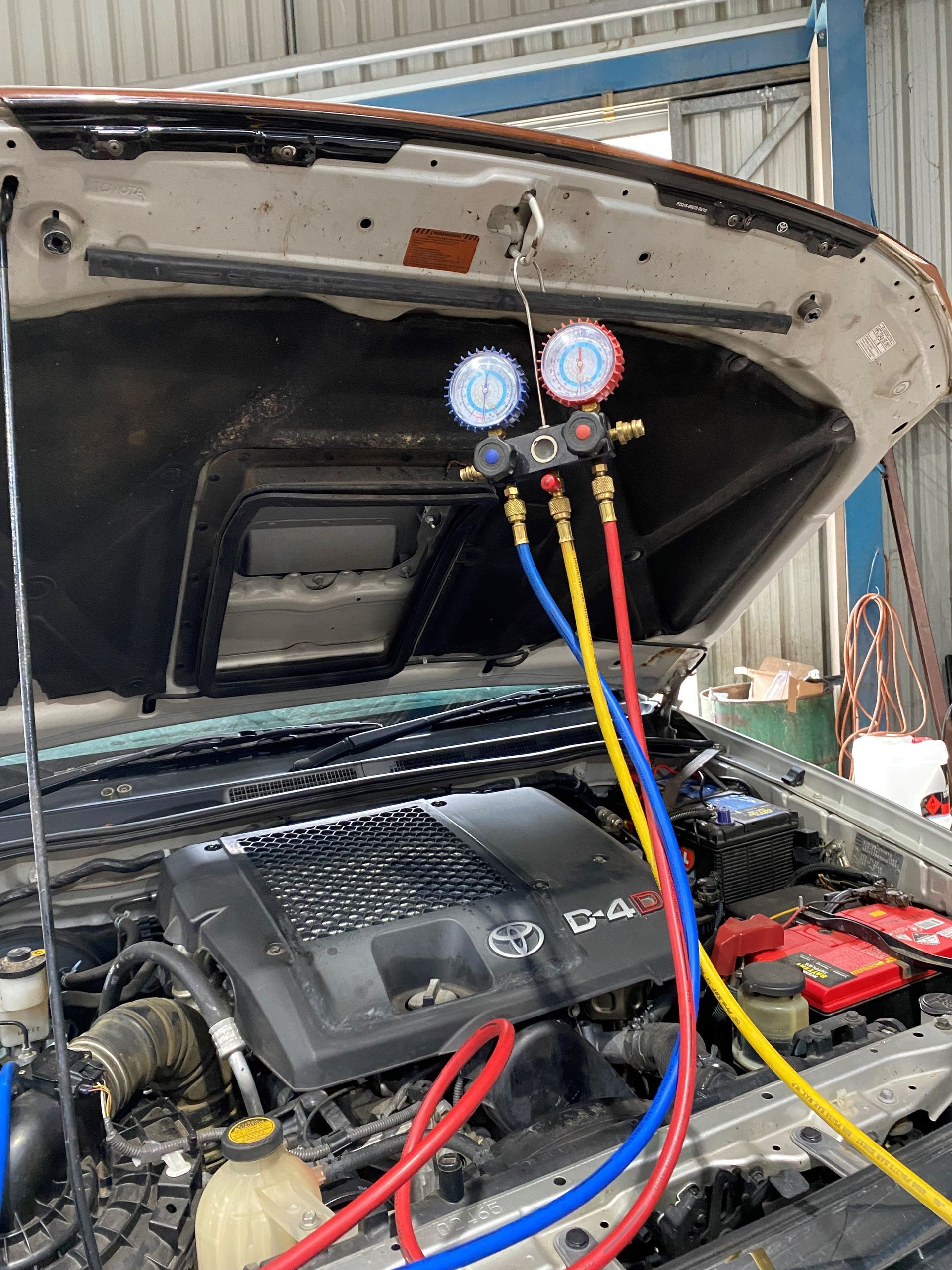 A car with the hood up is being serviced by a mechanic A man is looking under the hood of a car — Auto Air Conditioning in Wodonga, VIC