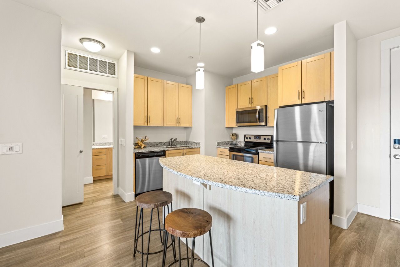 Open-concept kitchen with granite island, light wood cabinets, and stainless steel appliances.