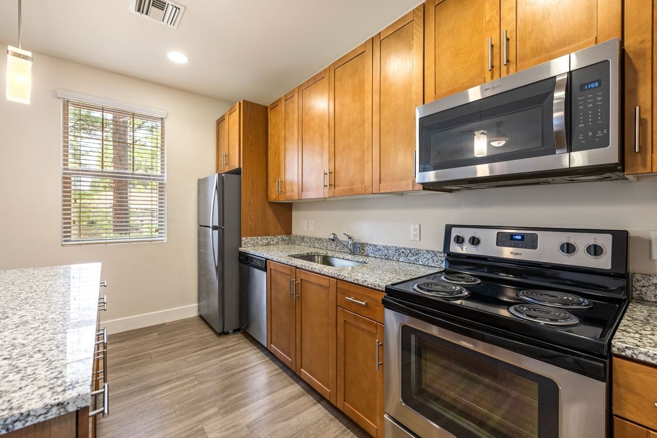 Modern apartment kitchen with granite countertops, wood cabinets, and stainless steel appliances.