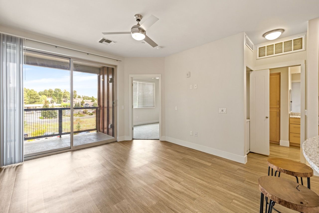 Living room with wood-style flooring, sliding glass doors to a balcony, and an open kitchen.