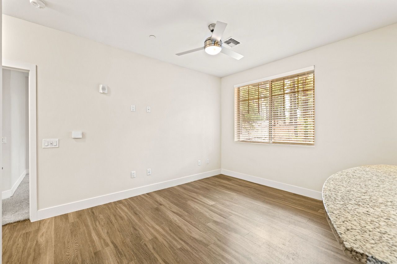 Empty apartment interior with wood floors, a window with blinds, and a curved granite countertop edge.