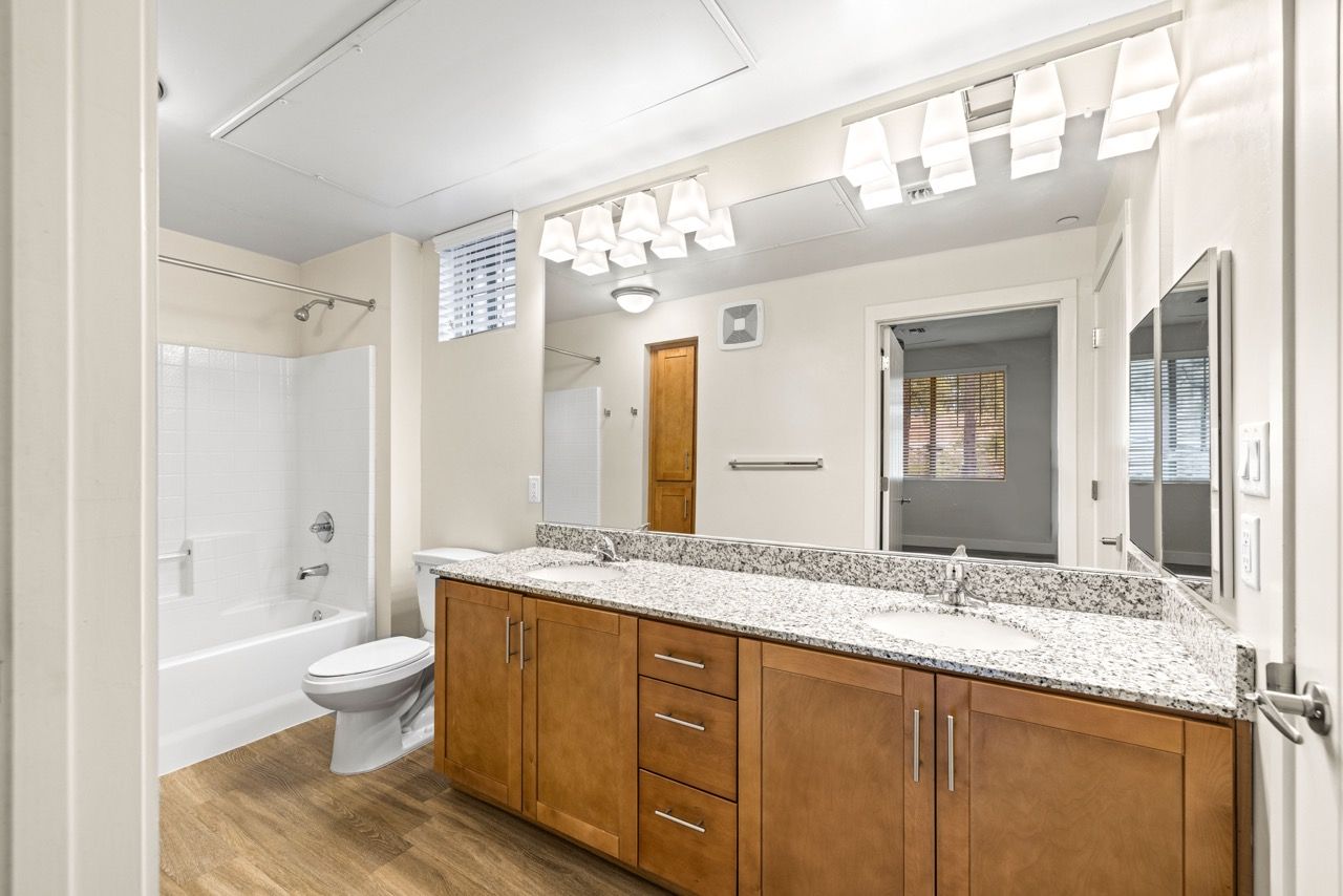 Bathroom with a double-sink vanity, granite countertop, wood cabinets, and a tub/shower combo.