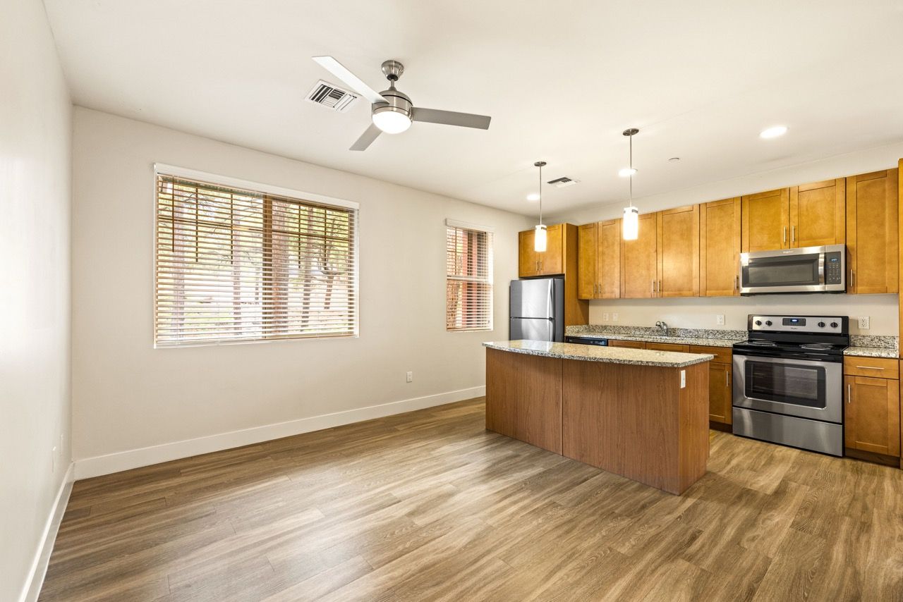 Open-concept kitchen with island, granite countertops, wooden cabinets, and stainless-steel appliances.