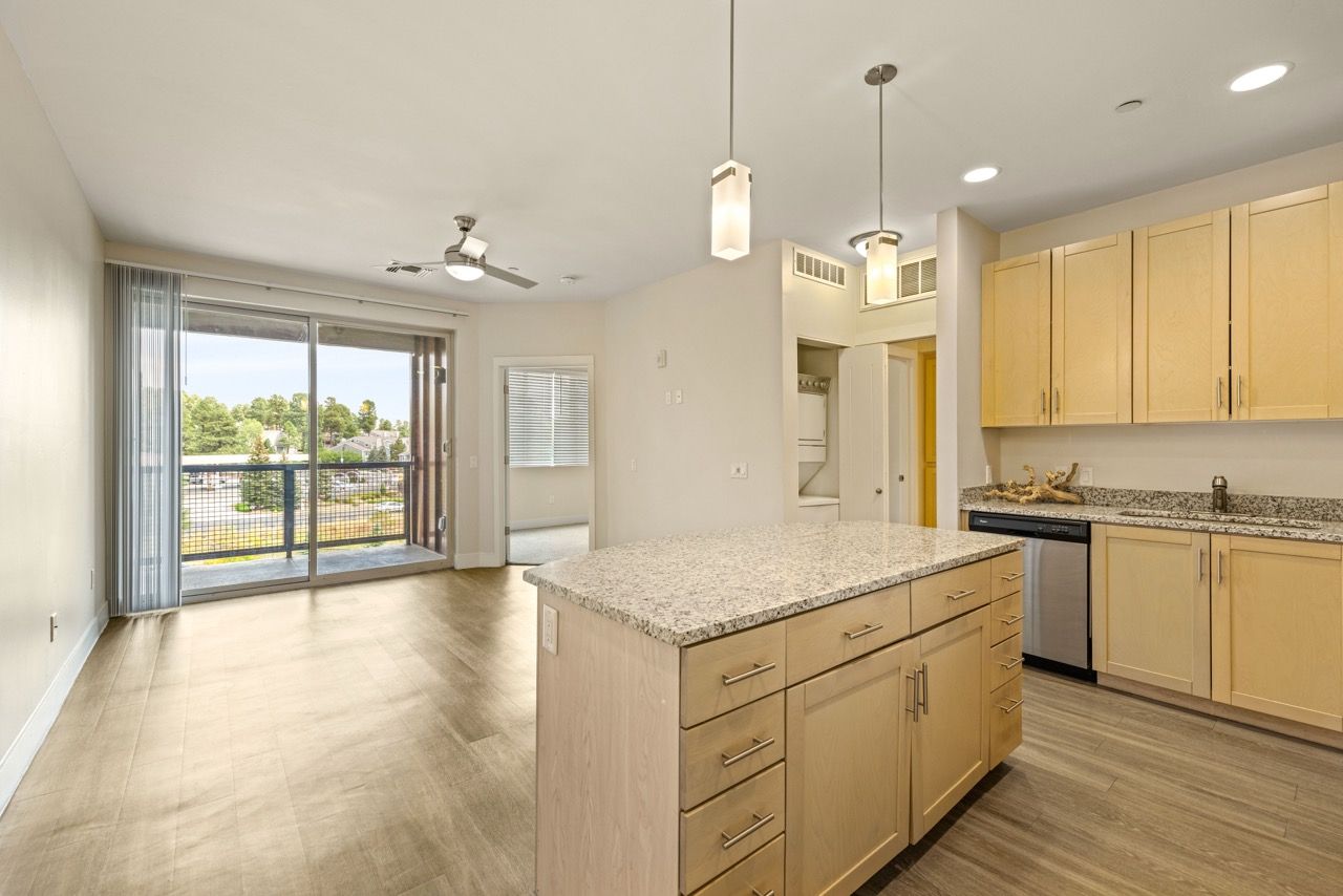 Open-concept kitchen with granite island, light wood cabinets, and a sliding glass balcony door.