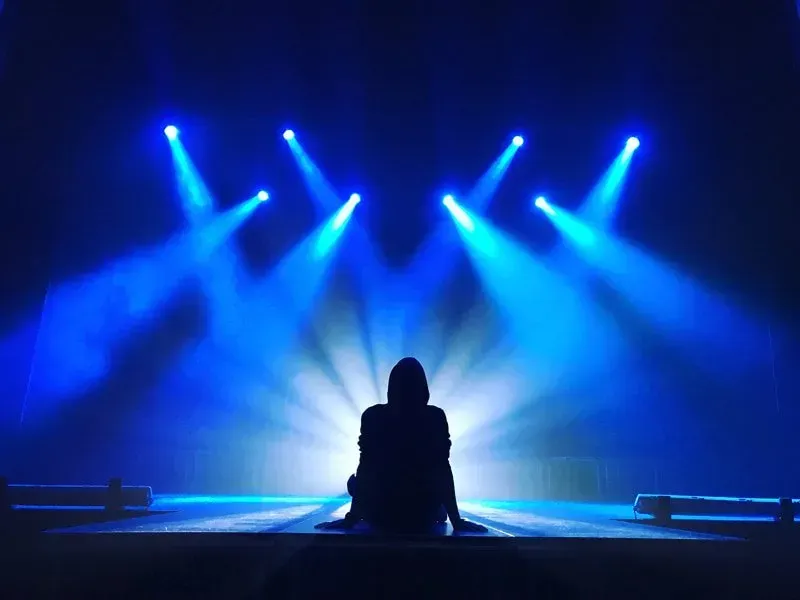 A person is sitting on a stage with blue lights behind them.