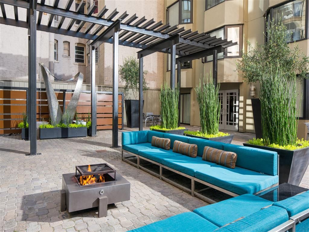Outdoor courtyard with blue cushioned seating, planters, and a fire pit under a pergola.