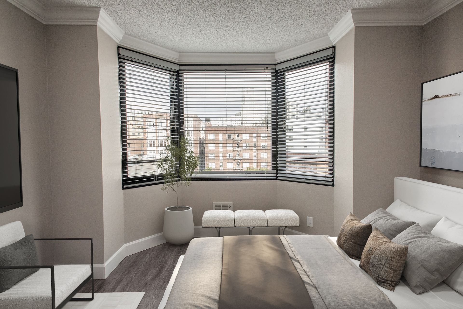 Bedroom with a curved bay window, horizontal blinds, a bed with neutral linens, and a small bench.