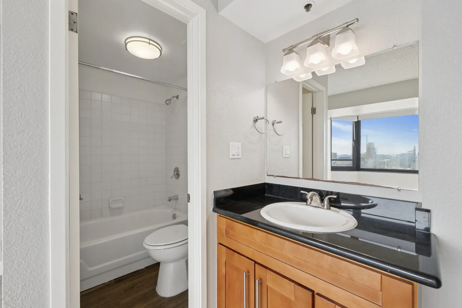 Bathroom vanity with black countertop, sink, and large mirror; tub/shower on left.