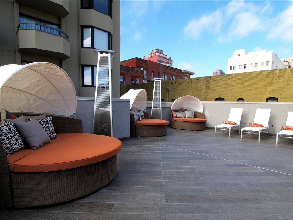 Rooftop terrace with curved wicker couches, orange cushions, and white sun loungers.