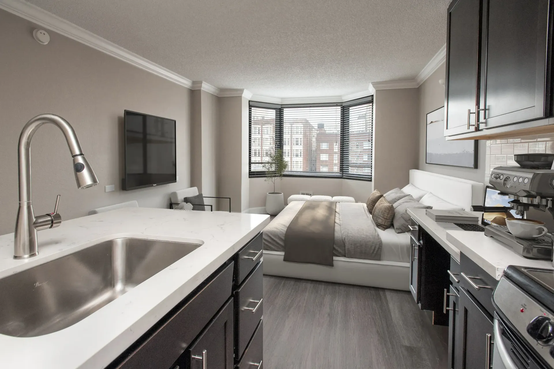 Open-concept kitchen and living area with a bed near a bay window and stainless sink.