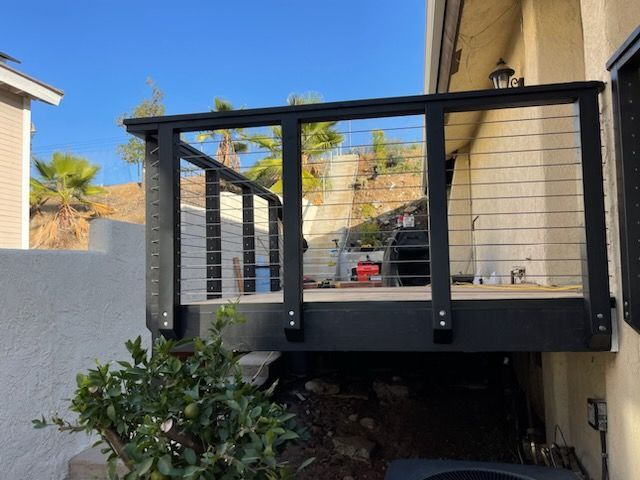 A black deck with a stainless steel railing is attached to the side of a house.