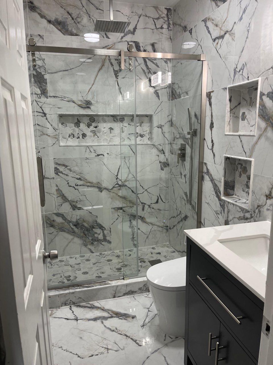 A bathroom with marble walls , a toilet , sink and shower.