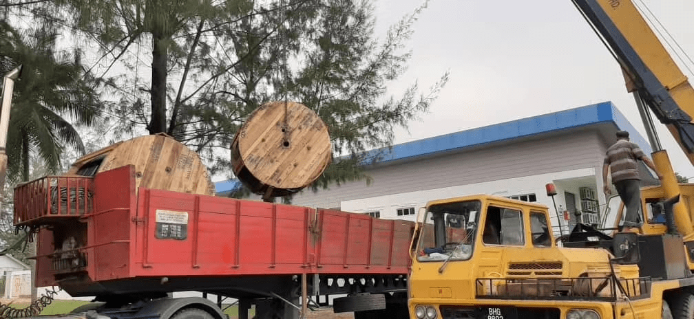 A truck is being loaded with large wooden cable spools by a crane.