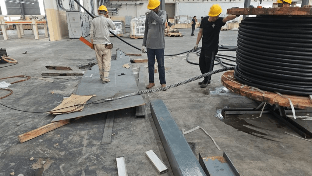 Workers wearing hard hats handling a large black cable spool in a warehouse.