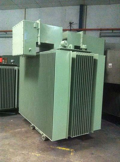 Green industrial transformer with corrugated sides, in a factory setting.