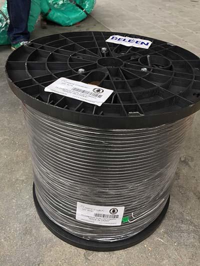 Black cable spool wrapped in clear plastic, on a gray surface.